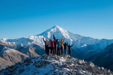 Group of trekkers raising hands in celebration on a snowy Himalayan mountain peak with a majestic mountain in the background.