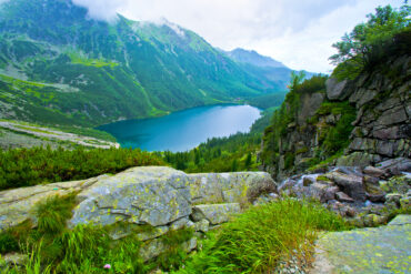 Scenic view of a mountain lake surrounded by lush green hills and rocky cliffs under a cloudy sky Himalayan Traveling.