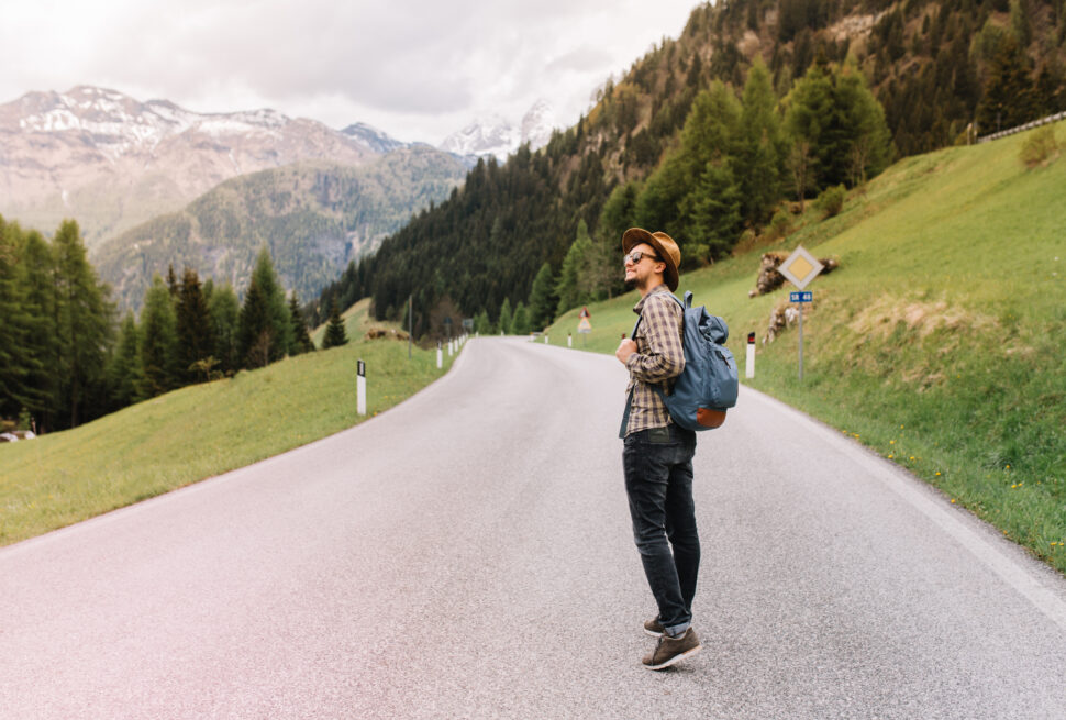 A young man on a solo mountain tour, standing on a road with the Alps in the background.