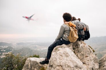 Travelers sitting on a mountain cliff watching an airplane fly by – experience guided by the Best Travel Agency.