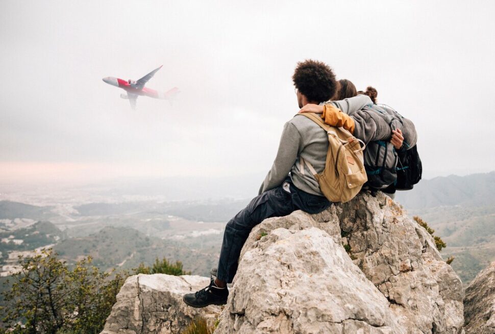 Travelers sitting on a mountain cliff watching an airplane fly by – experience guided by the Best Travel Agency.