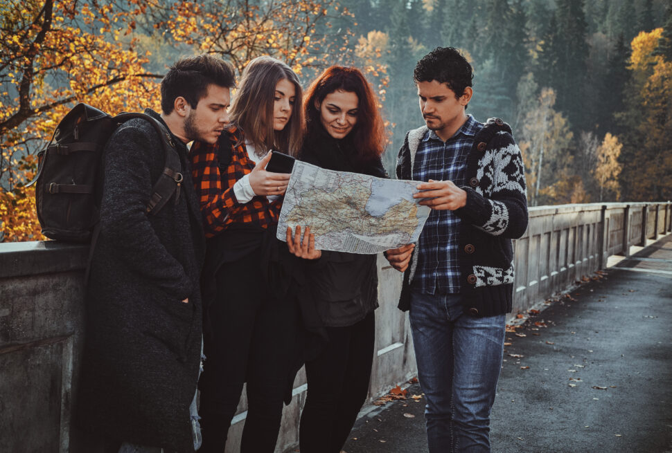 A group of four travelers standing outdoors and looking at a map while planning their journey with the help of a travel agent in Manali.